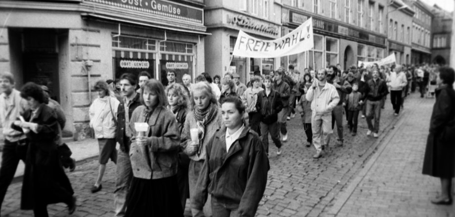 Demonstranten passieren die damalige Parchimer Straße des Friedens, auf ihren Transparenten werden freie Wahlen gefordert.